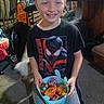 child, boy, smiling, indoor, bucket, candy, colorful, clothing, tshirt, kneeling, carpet, furniture, room, toy, happy, person, casual, home, spiderman, young