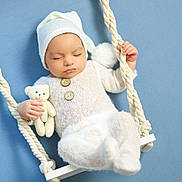 Badis a rejoint le concours — aidez-le/la à gagner de superbes lots ! baby, infant, sleeping, teddy_bear, white_clothing, knit_hat, swing, rope, blue_background, soft_texture, cute, peaceful, hand, footwear, portrait, child, indoors, toy, calm, resting