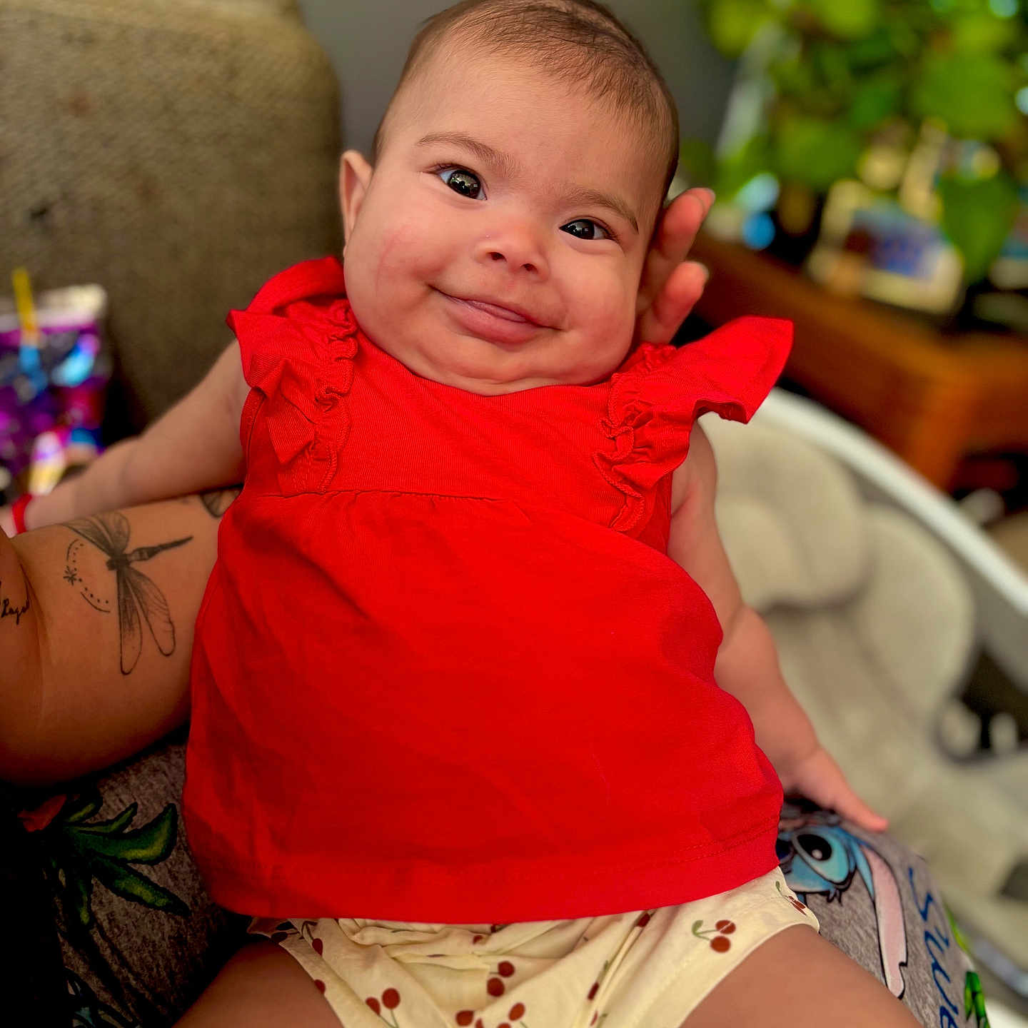 Avery joined the competition — help win amazing prizes! baby, child, smiling, red_clothing, tattoo, arm, indoor, plant, blurred_background, face, person, cute, happy, sitting, home, infant, skin, hand, short_hair, cheerful