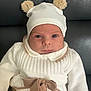 baby, child, infant, hat, bear_ears, sweater, bow, white_clothing, brown_clothing, cute, face, portrait, seated, indoor, leather_couch, warm_clothing, knitwear, expressionless, small_person, adorable