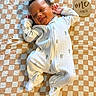 Roman is registered to the contest to win money with this photo: baby, smiling, onesie, cactus_print, blanket, checkered, wooden_sign, one_month, infant, cute, sleeping, happy, lying_down, indoors, human, newborn, portrait, soft_lighting, child, cozy