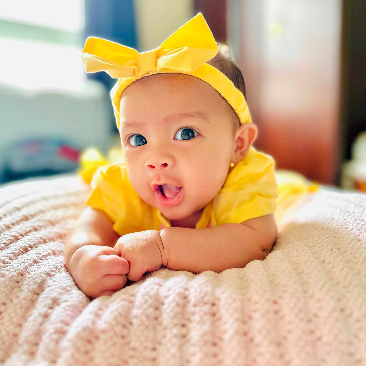 Elyzabelle Anya is registered to the contest to win money with this photo: adorable, baby, blanket, bright, child, closeup, cute, expression, face, hands, headband, indoors, infant, knitted, person, portrait, skin, soft, yellow_bow, young