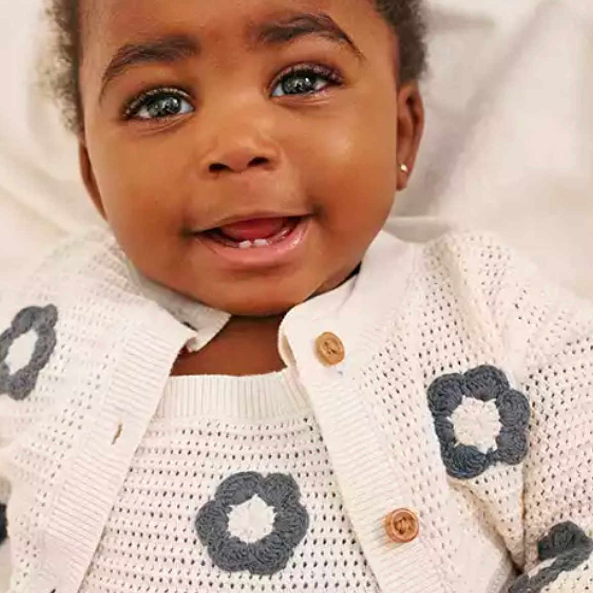 Salish is registered to the contest to win money with this photo: baby, child, closeup, cute, earring, eyes, face, flower_pattern, happy, indoors, infant, knitted_sweater, person, portrait, skin, smiling, soft_lighting, teeth, white_clothing, young