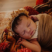 Giulia participe au concours pour gagner de l'argent avec cette photo : newborn, baby, sleeping, flower_crown, blanket, brown, red_flowers, cozy, soft_texture, portrait, infant, peaceful, wrapped, cute, close_up, indoor, decor, resting, child, warm_colors