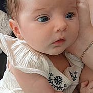 Arabella joined the competition — help win amazing prizes! baby, infant, child, close_up, face, eyes, hand, clothing, embroidery, skin, hair, portrait, soft_lighting, curious, expression, person, cradling, bracelet, indoors, caring
