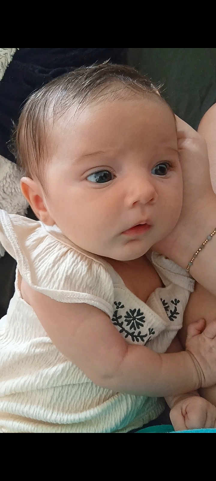 Arabella joined the competition — help win amazing prizes! baby, infant, child, close_up, face, eyes, hand, clothing, embroidery, skin, hair, portrait, soft_lighting, curious, expression, person, cradling, bracelet, indoors, caring