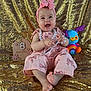 baby, child, smiling, pink_outfit, headband, pearl_necklace, toy, plush_toy, golden_sequin, milestone_sign, sitting, happy, portrait, indoors, cute, colorful, decorative, foot, hand, face