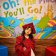 Leiza is registered to the contest to win money with this photo: child, graduation, gown, cap, pose, colorful, mural, illustration, hot_air_balloon, animal, celebration, smile, curly_hair, confident, indoor, wooden_wall, red, blue, yellow, green
