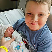 Troy joined the competition — help win amazing prizes! child, newborn, baby, smiling, hospital, blanket, blue_shirt, person, bed, wristband, hand, face, family, indoor, happy, sitting, holding, cute, newborn_hat, hospital_room