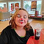 Alleah is registered to the contest to win money with this photo: child, sticker, face, silly, fast_food, restaurant, drink, table, cup, black_shirt, indoor, window, advertisement, poster, seat, hair, light, smile, casual, fun