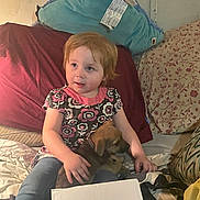 Morgan is registered to the contest to win money with this photo: child, puppy, bed, pillow, red_hair, jeans, floral_shirt, indoor, cute, pet, young_child, comfort, casual_clothing, home, animal, resting, curious, soft_lighting, cozy, person