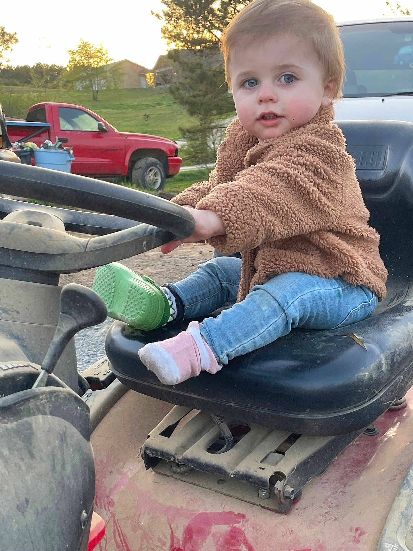 Wesson is registered to the contest to win money with this photo: child, toddler, lawn_mower, outdoor, grass, truck, steering_wheel, blue_eyes, jacket, denim_jeans, socks, green_shoe, sunset, dirt, seat, person, vehicle, nature, playful, cute