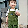 Enzo Calero Cepeda is registered to the contest to win money with this photo: child, toddler, curly_hair, portrait, standing, outdoor, patio, overalls, green_clothing, corduroy, white_shirt, looking_away, neutral_expression, face, eyes, window, chair, tiled_floor, daylight, casual_photo