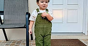 Enzo Calero Cepeda joined the competition — help win amazing prizes! child, toddler, curly_hair, portrait, standing, outdoor, front_door, house, patio, chair, overalls, green_clothing, white_shirt, shoes, tile_floor, doormat, window, home, smiling, full_body