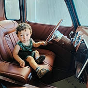 Enzo Calero Cepeda is registered to the contest to win money with this photo: toddler, child, baby, vintage_car, car_interior, driver_seat, steering_wheel, dashboard, leather_seat, chrome, curly_hair, portrait, sitting, looking_at_camera, green_outfit, shoes, automobile, indoor, photography, cute