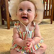 Bernadette joined the competition — help win amazing prizes! baby, child, smiling, hat, colorful_clothing, carpet, indoor, furniture, crib, happy, cute, portrait, sitting, infant, person, baby_clothes, room, skin, hands, feet