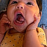 Ailani is registered to the contest to win money with this photo: baby, infant, child, portrait, wide_eyed, open_mouth, surprised, sitting, indoor, close_up, face, hands, arms, polka_dot, yellow_outfit, denim, couch, warm_lighting, adorable, photograph