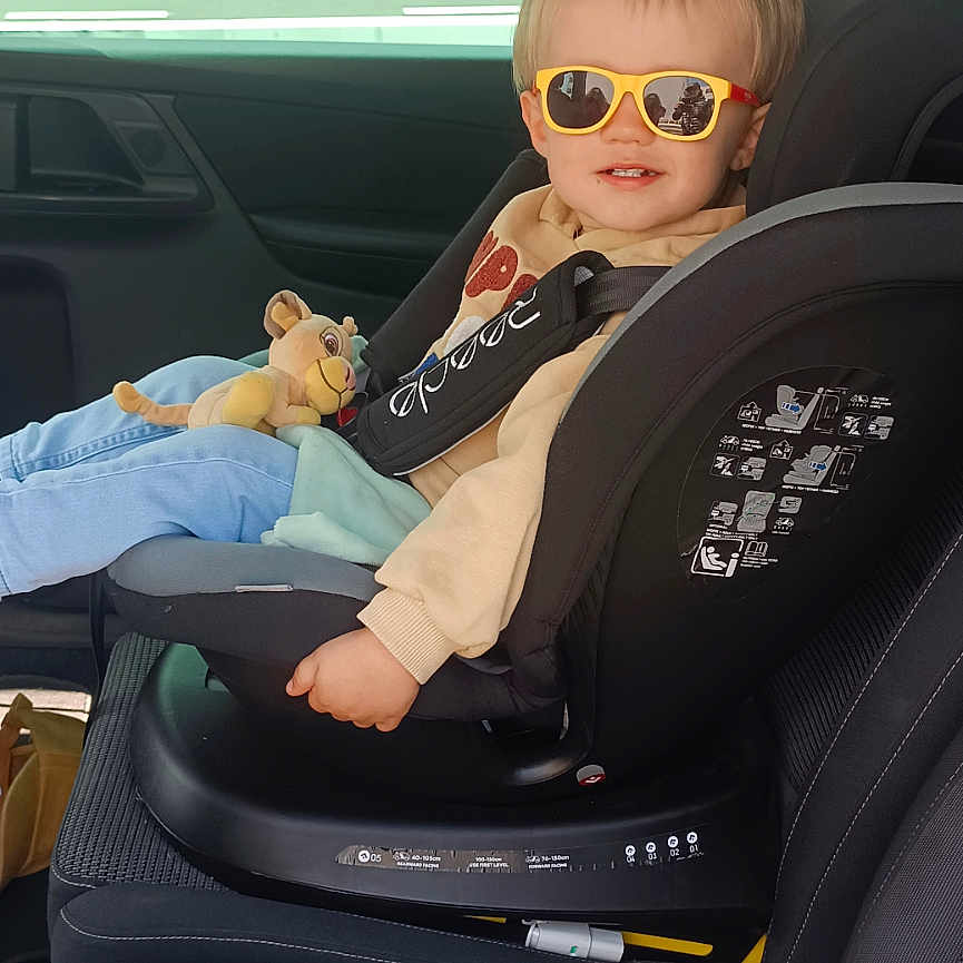 Iron a rejoint le concours — aidez-le/la à gagner de superbes lots ! beige_sweatshirt, car_interior, car_seat, casual_clothing, child, head, light_blue_jeans, lion_toy, plush_toy, reflection, safety, seat, seatbelt, sitting, smile, sunglasses, sunlight, toddler, vehicle, window