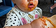 Quinn is registered to the contest to win money with this photo: toddler, child, messy, spaghetti, food, bib, high_chair, restaurant, indoor, face, hand, clothing, table, plate, sauce, eating, person, hair, expression, seat