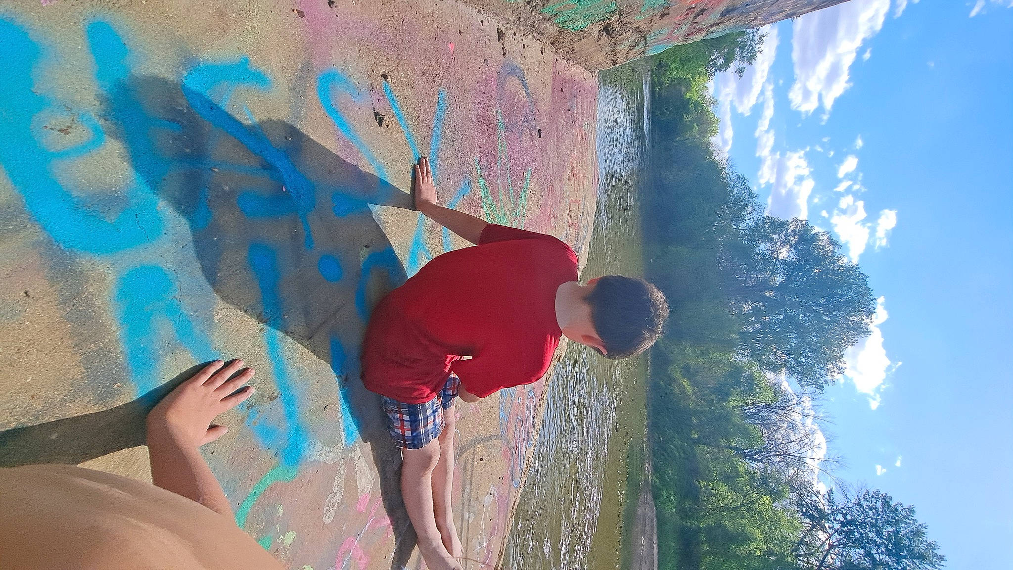 Kayleb is registered to the contest to win money with this photo: adventure, arm, art, azure, climbing, electric_blue, fun, leisure, mural, person, plant, recreation, rock, shorts, sky, sport_climbing, t_shirt, tree, visual_arts, water