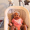 baby, infant, smiling, pink_clothing, headband, baby_seat, cushion, patterned_fabric, star_toys, mobile, indoor, carpet, happy, child, cute, baby_bib, baby_girl, playful, seated, comfort