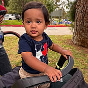 Elijah joined the competition — help win amazing prizes! toddler, child, stroller, outdoor, park, grass, tree, person, clothing, hand, face, expression, curious, casual, daylight, young_child, nature, walk, baby, portrait