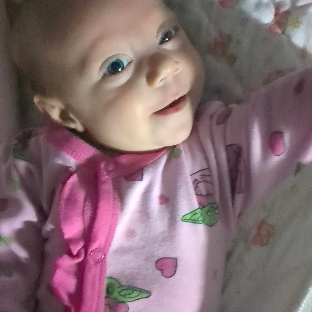 Nova joined the competition — help win amazing prizes! baby, child, infant, smiling, face, portrait, lying_down, crib, bedding, floral, pink_clothing, pajamas, romper, indoor, nursery, happy, blue_eyes, baby_bed, blanket, photography