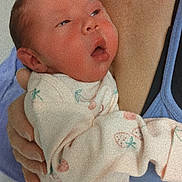 Nova is registered to the contest to win money with this photo: newborn, baby, infant, child, face, eyes, open_mouth, sleepy, portrait, person, held, cradled, adult_arm, onesie, clothing, fruit_pattern, blanket, indoor, closeup, text_overlay