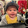 baby, child, shopping_cart, cap, smile, clothing_store, jacket, yellow_shirt, rack, shopping, happy, face, retail, apparel, infant, store_interior, cute, person, headwear, casual_wear