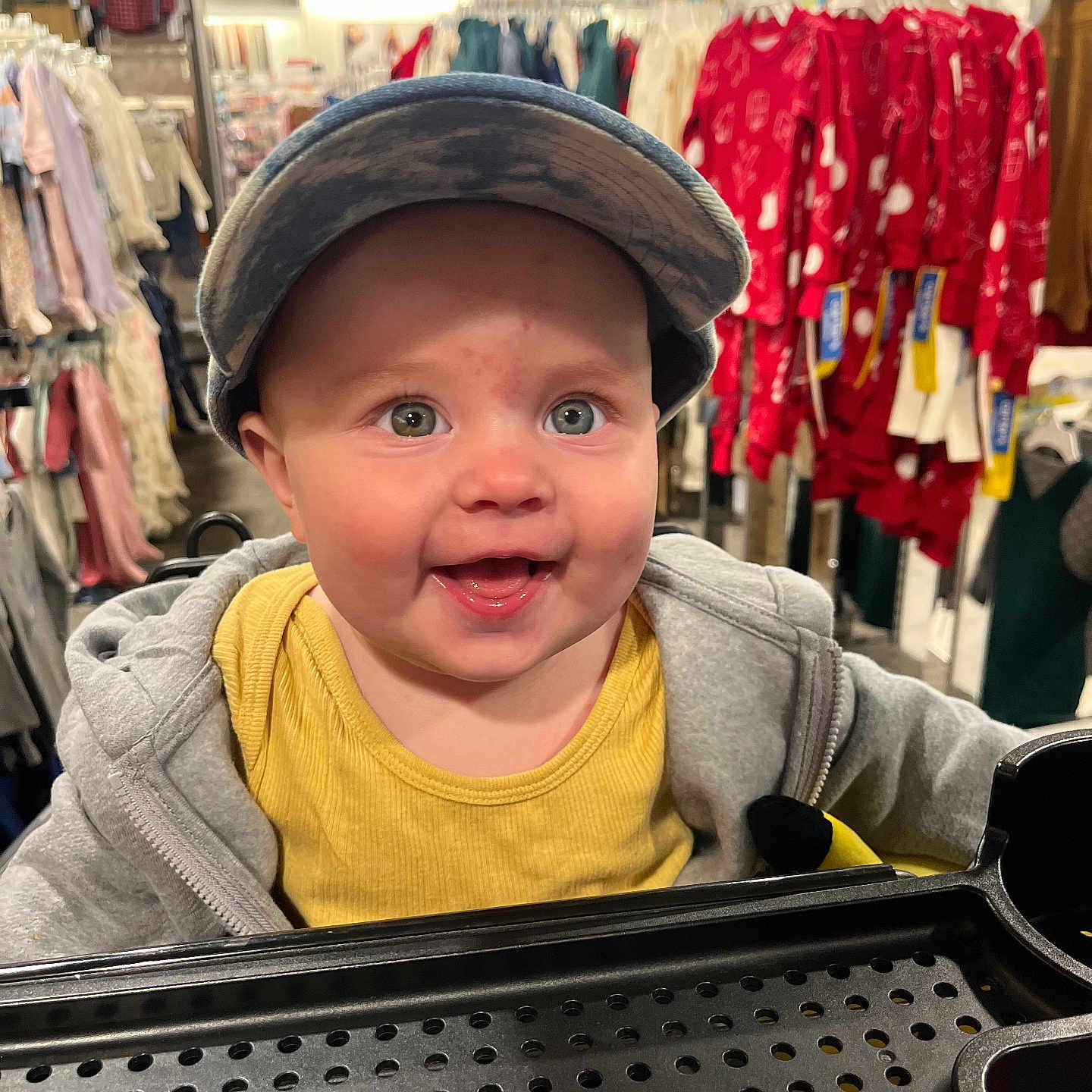 Ryatt joined the competition — help win amazing prizes! apparel, baby, cap, casual_wear, child, clothing_store, cute, face, happy, headwear, infant, jacket, person, rack, retail, shopping, shopping_cart, smile, store_interior, yellow_shirt