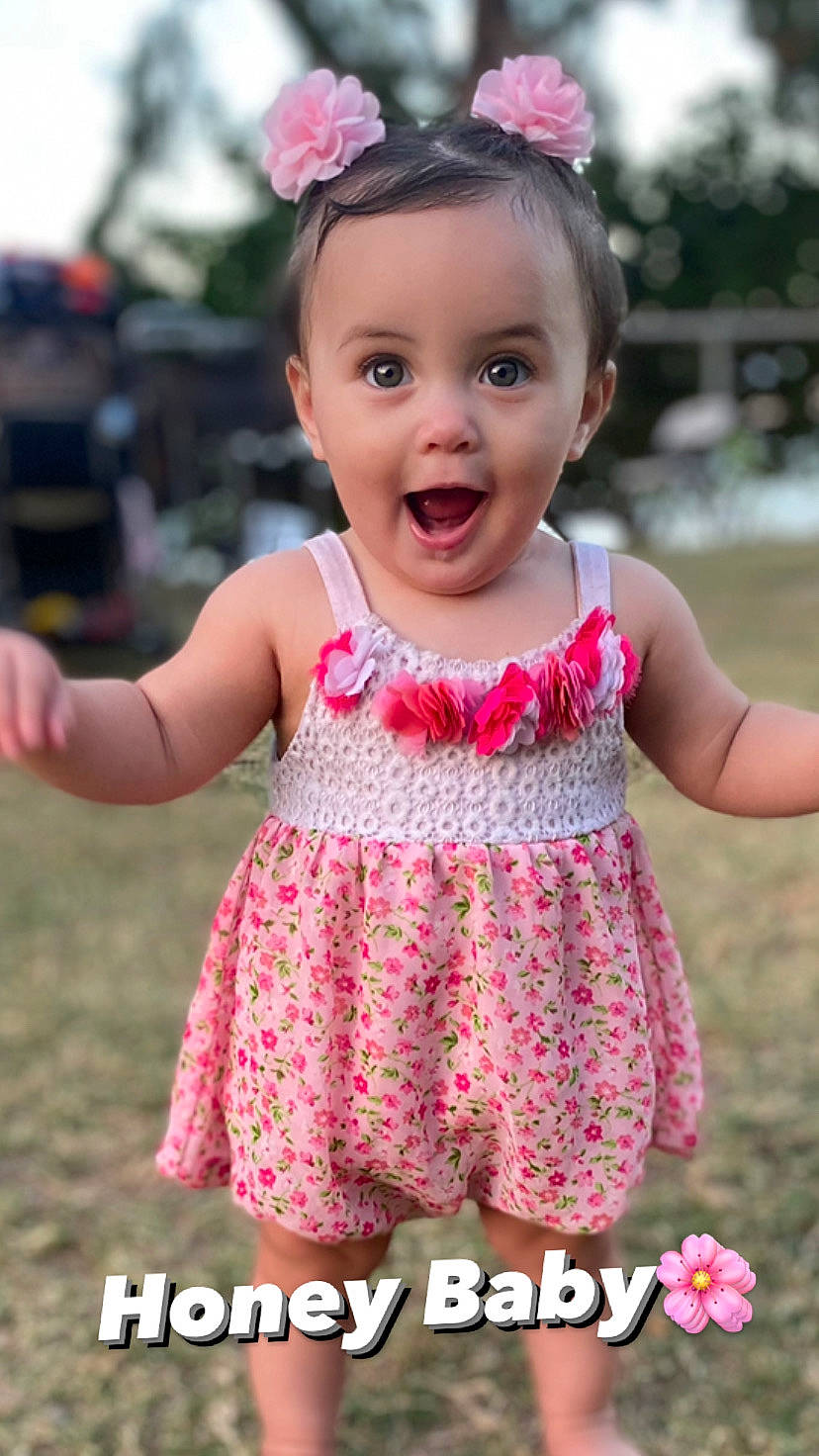 Honey is registered to the contest to win money with this photo: baby, baby_toddler_clothing, clothing, dress, eye, finger, grass, green, happy, iris, person, photograph, pink, plant, purple, skin, sleeve, smile, surprise, toddler