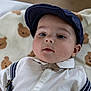 baby, child, face, cap, hat, bow_tie, shirt, suspenders, blanket, teddy_bear_pattern, infant, cute, portrait, lying_down, indoor, clothing, young_child, expression, closeup, headwear