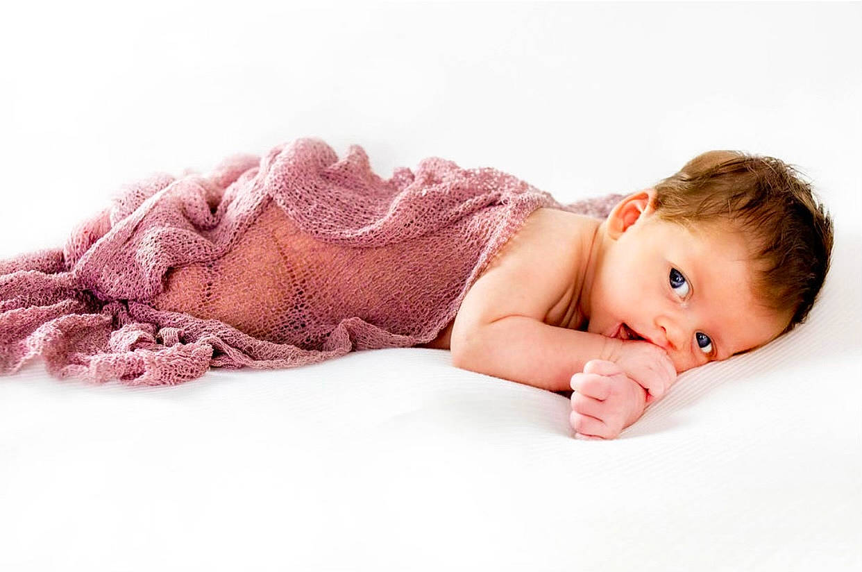 Bristol is registered to the contest to win money with this photo: baby, baby_toddler_clothing, comfort, dress, eye, fashion_accessory, flooring, foot, human_leg, linens, lip, pattern, person, pink, sitting, skin, sleeve, textile, toddler, tummy_time