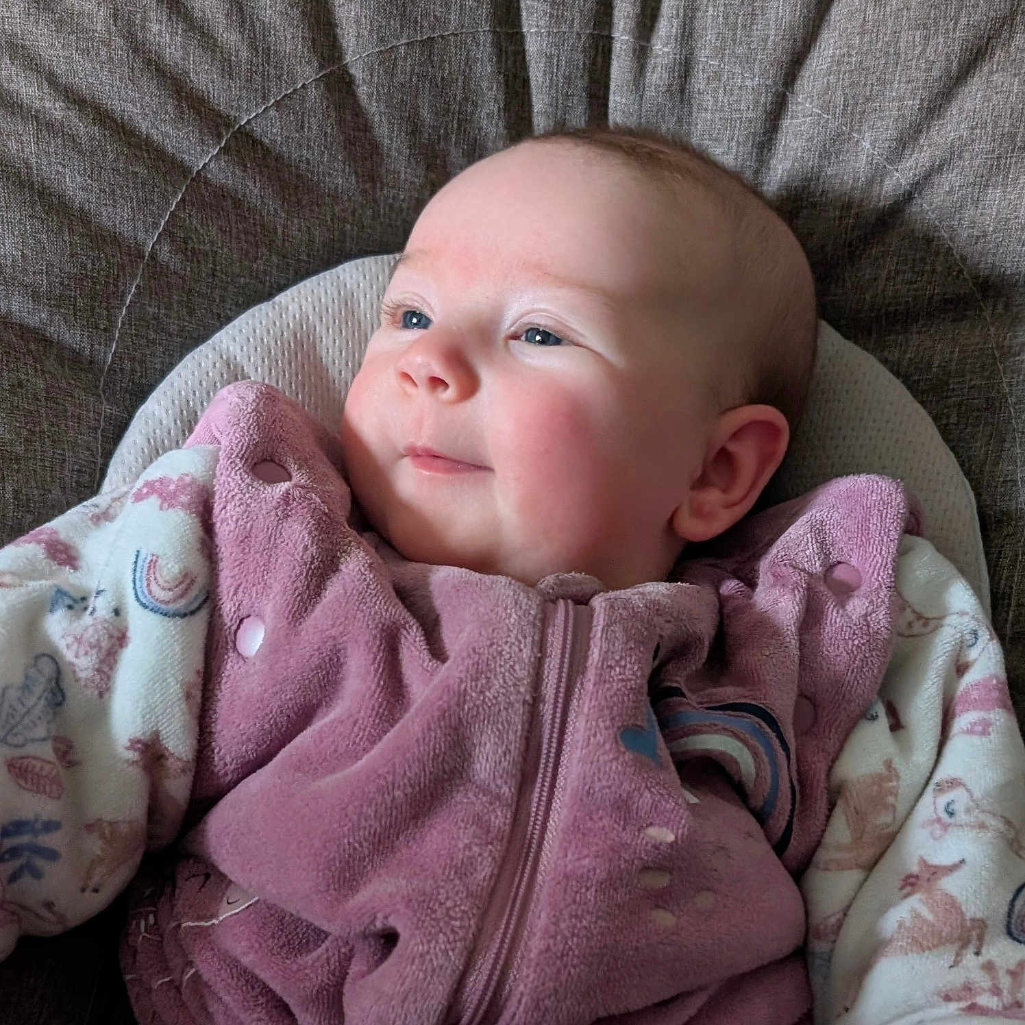 Hénora a rejoint le concours — aidez-le/la à gagner de superbes lots ! animal_pattern, baby, child, closeup, cozy, cushion, cute, ears, fabric_texture, face, head, indoor, infant, patterned_clothing, pink_clothing, portrait, rainbow_pattern, seated, smile, soft_lighting