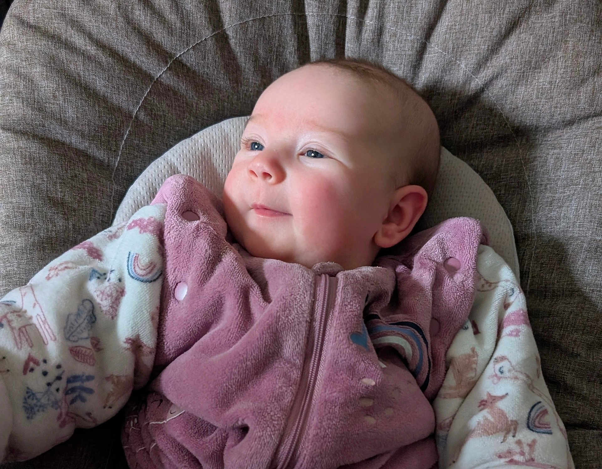 Hénora a rejoint le concours — aidez-le/la à gagner de superbes lots ! baby, infant, child, pink_clothing, patterned_clothing, rainbow_pattern, animal_pattern, smile, face, head, ears, cushion, fabric_texture, seated, closeup, soft_lighting, indoor, portrait, cute, cozy