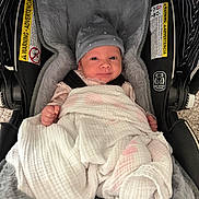 Alina is registered to the contest to win money with this photo: baby, infant, car_seat, blanket, hat, clothing, face, person, indoor, soft_texture, stripes, warning_label, cushion, cute, newborn, wrapped, smile, small_fist, headwear, fabric