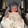baby, infant, car_seat, blanket, hat, clothing, face, person, indoor, soft_texture, stripes, warning_label, cushion, cute, newborn, wrapped, smile, small_fist, headwear, fabric