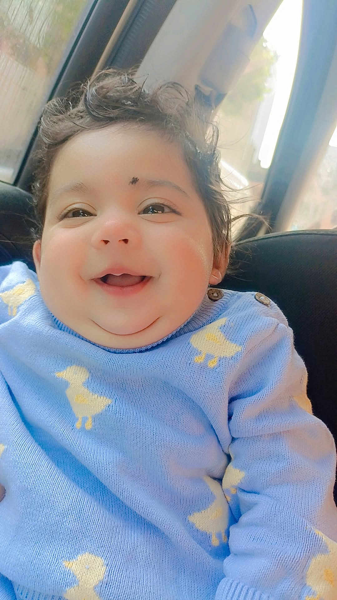 Gurviraat Singh is registered to the contest to win money with this photo: baby, child, smiling, curly_hair, blue_sweater, yellow_ducks, car_seat, indoors, natural_light, happy, cute, portrait, face, clothing, cozy, infant, sitting, soft_light, closeup, person