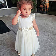 Kaylani Williams joined the competition — help win amazing prizes! toddler, child, white_dress, bow, curly_hair, pearl_necklace, gold_shoes, outdoor, concrete, sidewalk, thoughtful, standing, portrait, cute, fashion, person, young_child, daylight, expression, small_child