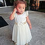 toddler, child, white_dress, bow, curly_hair, pearl_necklace, gold_shoes, outdoor, concrete, sidewalk, thoughtful, standing, portrait, cute, fashion, person, young_child, daylight, expression, small_child
