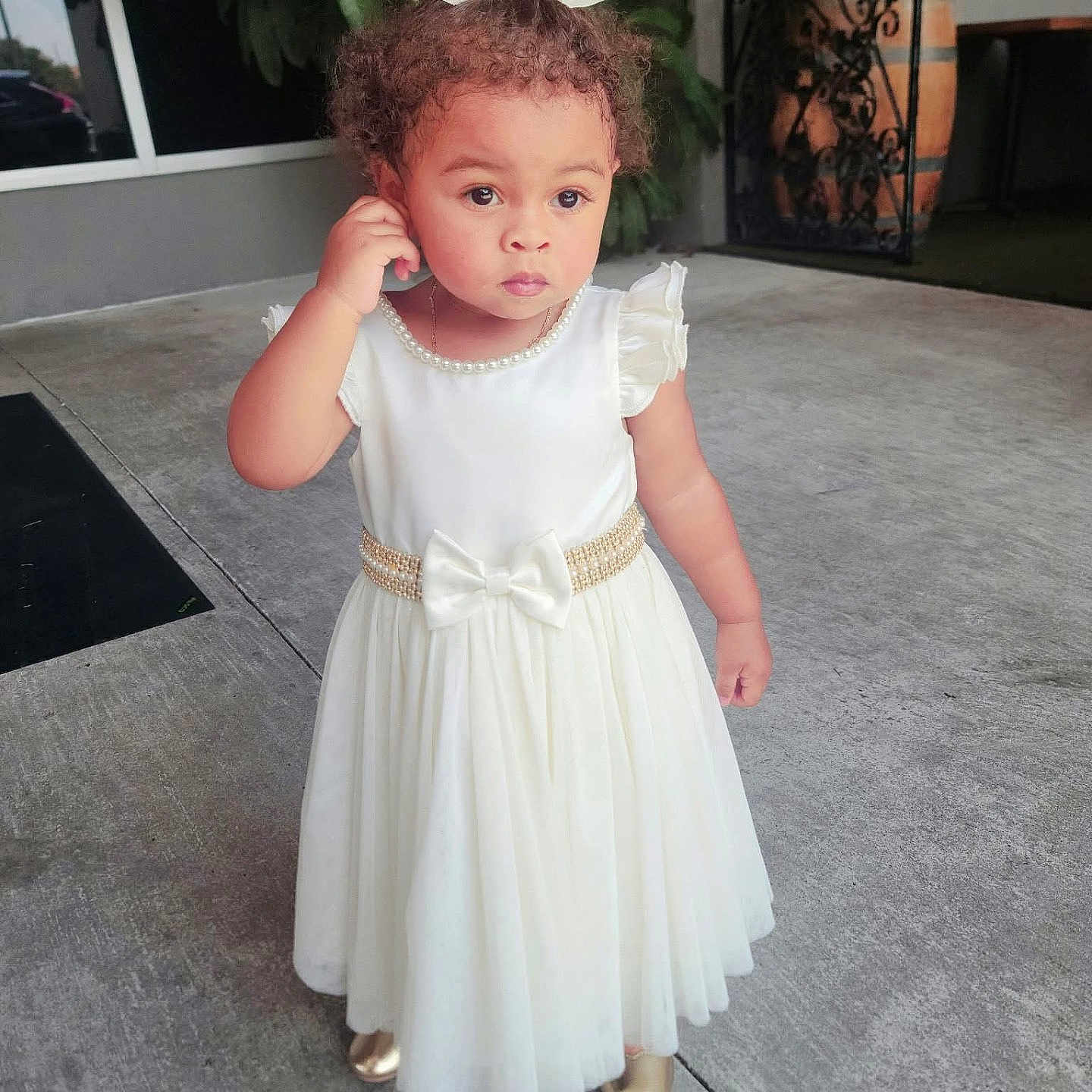 Kaylani Williams joined the competition — help win amazing prizes! bow, child, concrete, curly_hair, cute, daylight, expression, fashion, gold_shoes, outdoor, pearl_necklace, person, portrait, sidewalk, small_child, standing, thoughtful, toddler, white_dress, young_child