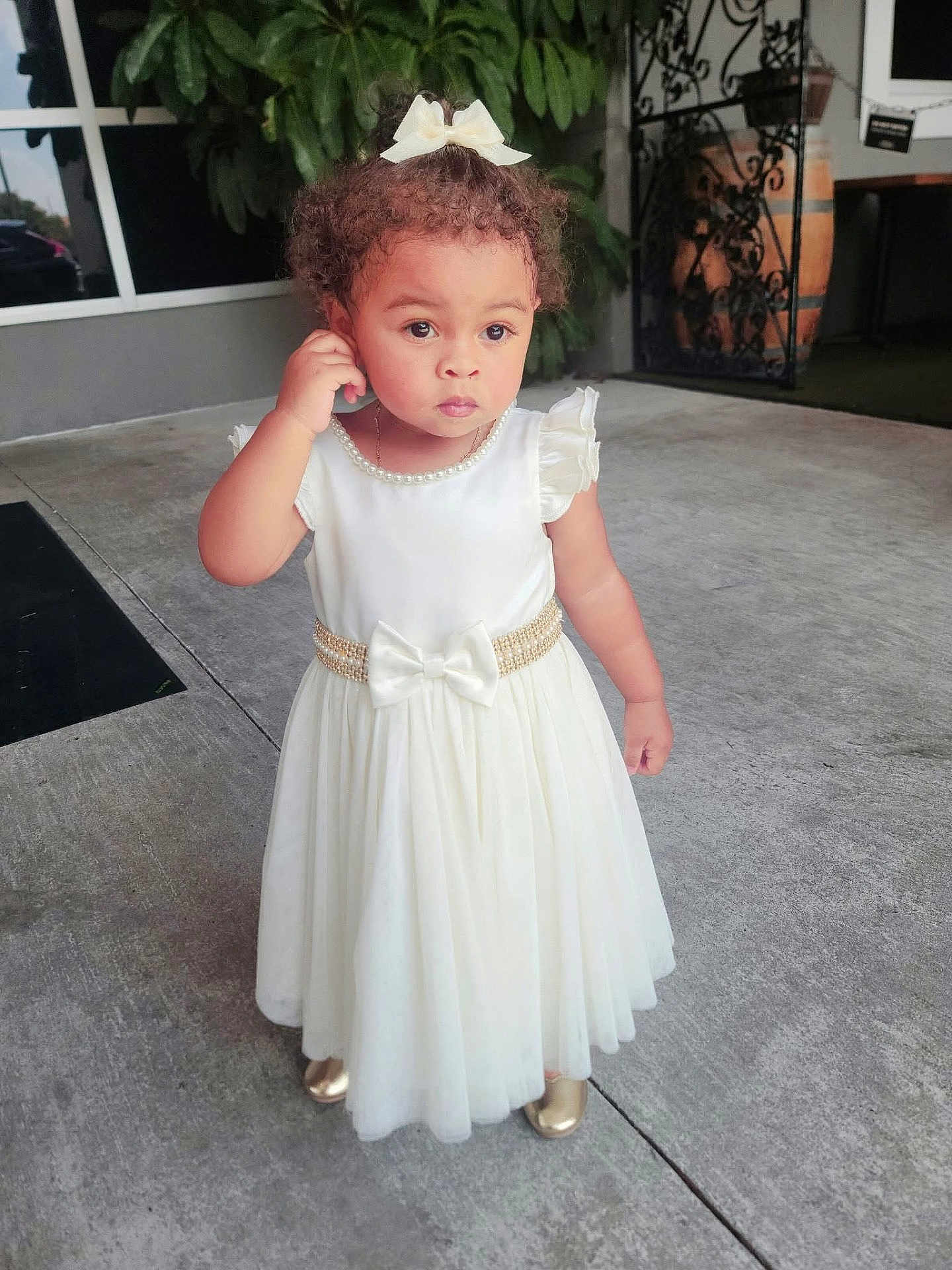 Kaylani Williams joined the competition — help win amazing prizes! toddler, child, white_dress, bow, curly_hair, pearl_necklace, gold_shoes, outdoor, concrete, sidewalk, thoughtful, standing, portrait, cute, fashion, person, young_child, daylight, expression, small_child