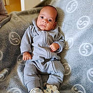Tyano a rejoint le concours — aidez-le/la à gagner de superbes lots ! baby, infant, onesie, grey_clothing, blanket, soft_texture, dinosaur_shoes, footwear, indoor, curious_expression, lying_down, cozy, child, cute, small_hands, patterned_blanket, comfortable, portrait, wide_eyes, young_child