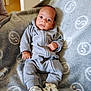 baby, infant, onesie, grey_clothing, blanket, soft_texture, dinosaur_shoes, footwear, indoor, curious_expression, lying_down, cozy, child, cute, small_hands, patterned_blanket, comfortable, portrait, wide_eyes, young_child