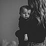 baby, child, woman, holding, black_and_white, portrait, indoor, curly_hair, person, clothing, face, back_view, casual, jeans, intimate, expression, close_up, soft_light, emotional, family