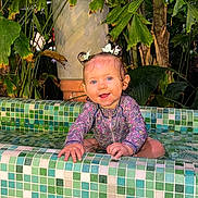 Maria a rejoint le concours — aidez-le/la à gagner de superbes lots ! baby, blue_eyes, bows, child, cute, floral_swimsuit, greenery, happy, outdoor, pigtails, plants, playful, pool, portrait, sitting, smiling, tiled_pool, toddler, water, wet_hair