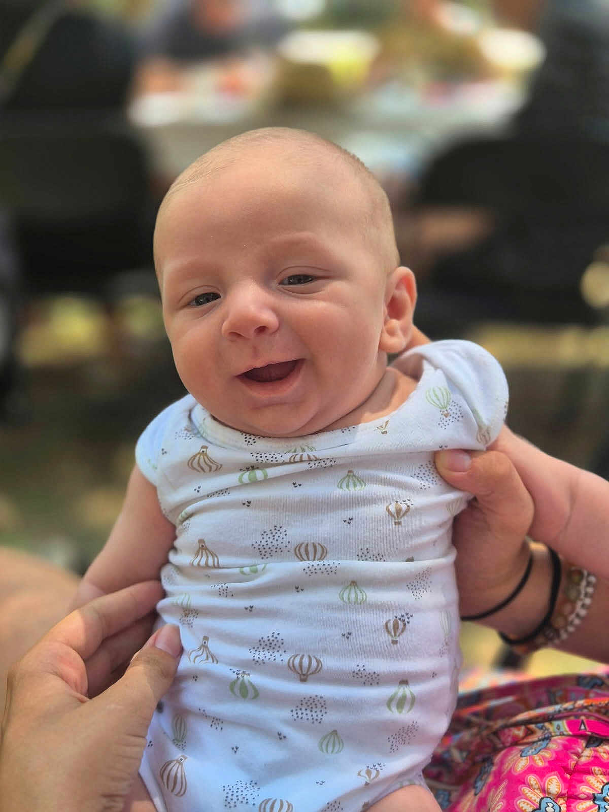 Loan a rejoint le concours — aidez-le/la à gagner de superbes lots ! baby, infant, smile, happy, person, onesie, patterned_clothing, hand, holding, portrait, close_up, child, cute, outdoor, blurred_background, people, skin, head, face, expression