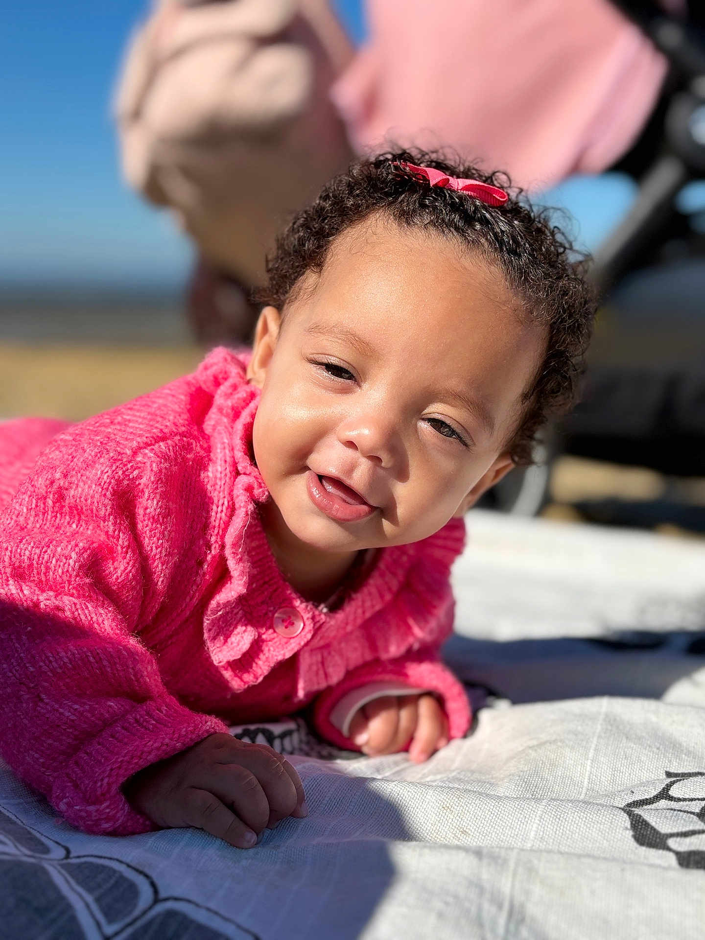 Tyanah a rejoint le concours — aidez-le/la à gagner de superbes lots ! baby, blanket, bow, child, close_up, curly_hair, cute, daylight, face, happy, infant, outdoor, person, pink_sweater, portrait, skin, smiling, sunlight, warm_clothing, young_child