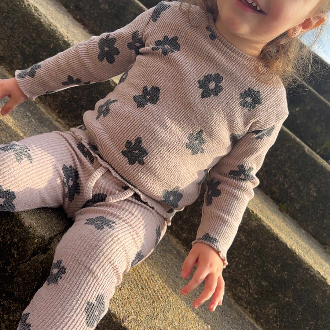 Layana participe au concours pour gagner de l'argent avec cette photo : child, toddler, smiling, sitting, outdoor, steps, concrete, clothing, floral_pattern, pink_shoes, sunlight, shadow, face, happy, person, casual_wear, daylight, building, sky, earrings