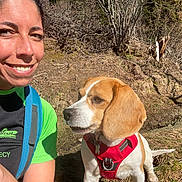 Daisy a rejoint le concours — aidez-le/la à gagner de superbes lots ! person, dog, beagle, red_harness, smile, outdoor, nature, trees, grass, trail, sunlight, backpack, portrait, face, companionship, pet, hiking, floppy_ear, snout, happy